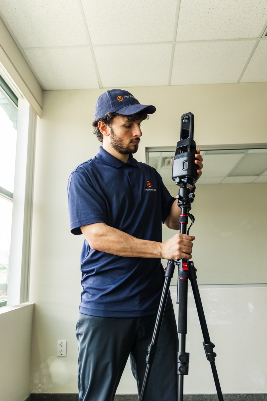 PlanBase 360 operator adjusting a tripod-mounted LiDAR scanner beside a full-height commercial window