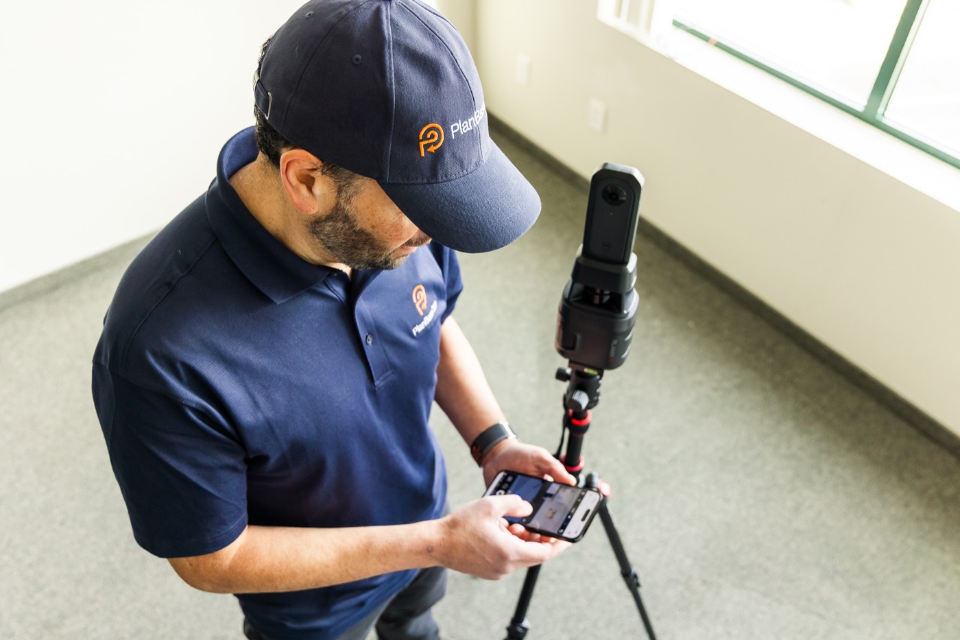 Overhead view of a PlanBase 360 operator checking scan progress beside a tripod-mounted scanner in a commercial interior