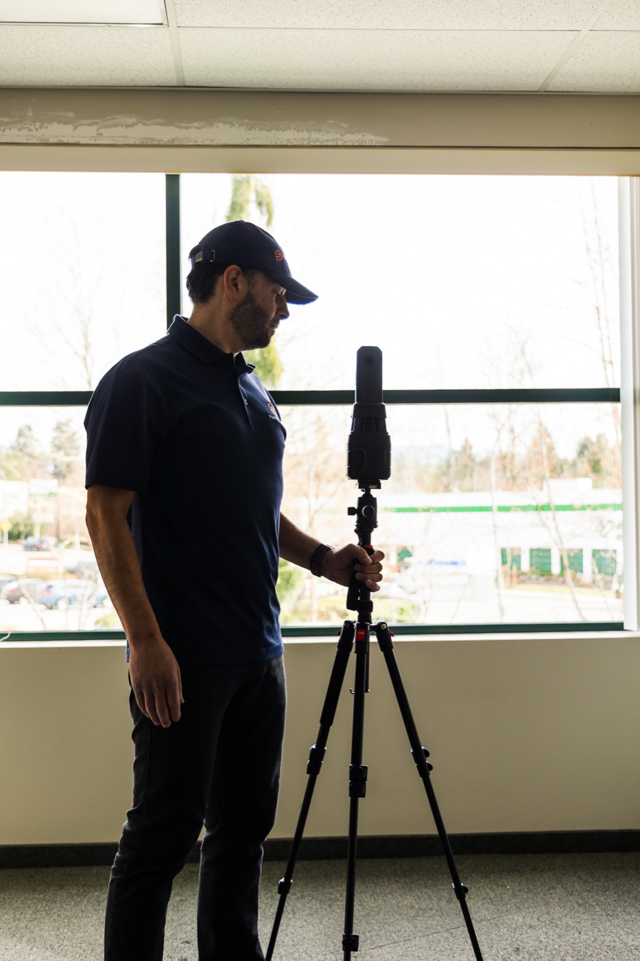 PlanBase 360 operator scanning a commercial interior with a tripod-mounted LiDAR scanner beside a full-height window